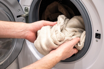 A man puts a beige acrylic sweatshirt into the washing machine for washing