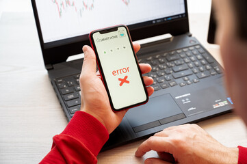 Man holding a smartphone displaying a smart home error message, sitting at a desk with a laptop in...
