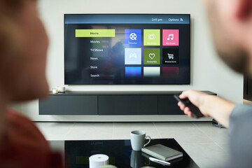Two people using remote control while seated and facing smart TV displaying various options on...