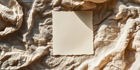 Blank paper sheet card positioned on a crumpled beige bed blanket, creating a mockup copy space. The soft warm sunlight shadows enhance the aesthetic minimal brand template in this flat lay setup.