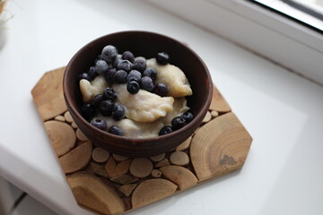 Sweet dumplings (vareniki) topped with frozen blueberries, served in a rustic wooden bowl. The cozy winter setting emphasizes warmth and comfort, making it perfect for food photography or traditional 