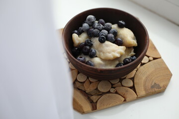 Sweet dumplings (vareniki) topped with frozen blueberries, served in a rustic wooden bowl. The cozy winter setting emphasizes warmth and comfort, making it perfect for food photography or traditional 