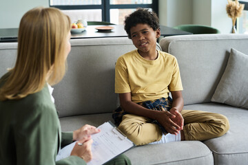 Young boy sitting on couch during therapy session interacting with therapist without distractions....