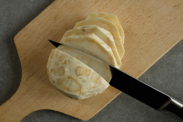 Celery root sliced with a knife on a cutting board.