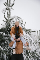 A cheerful couple enjoys a snowy winter day, with the woman playfully sitting on the man's shoulders amidst snow-covered pine trees. The scene captures warmth and joy against a serene, white backdrop.