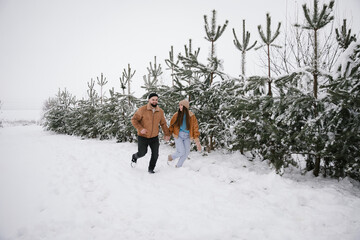 A couple in love are running through the snow in a snowy pine forest.	
