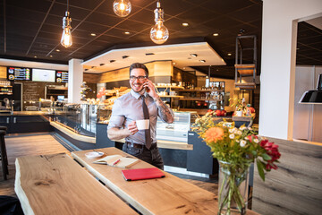 Junger Business Mann im Café arbeitet mit Laptop und Telefon produktiv in einem modernen...