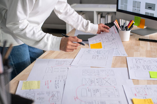 UX UI designer working on wireframes for a website and mobile app prototype, surrounded by sketches of user-flow and design tools, in concept of website and mobile application design concept. - Powered by Adobe