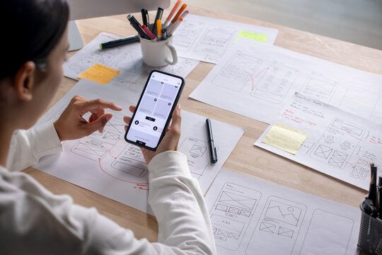 UX UI designer testing prototype on a phone, discussing and brainstorming on wireframes for a website and mobile app prototype, in the concept of website and mobile application design concept.