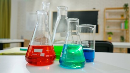 Empty school chemistry classroom with desks, chairs and chalkboard, workspace for teaching and studying. Glass bottles with colorful liquids close up.