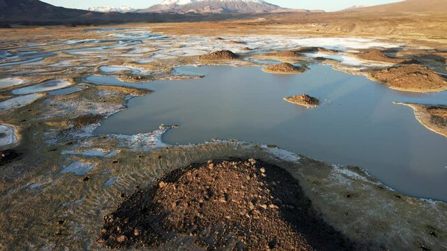 Aerial Drone Footage Captures Lauca National Park In Chile During A Sunny Autumn Day. The Camera Pans Over Small Hills And Lakes, Revealing The Snow-Capped Vulcan Parinacota At Sunset.