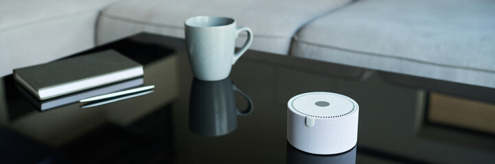 Reflecting cozy workspace with a smart speaker, notebook, pen and coffee mug on a glass table. Modern minimalist design and efficient gadgets for productivity