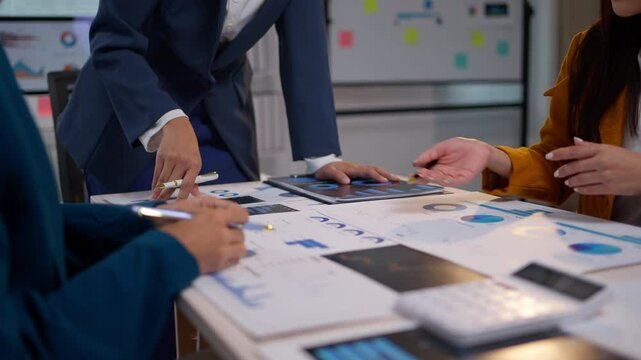 Businesswomen collaborating in a meeting room, analyzing financial graphs and charts on their desks