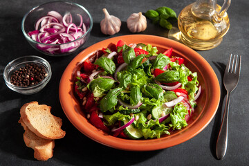 Fresh salad with tomatoes, cucumbers, onions, basil and pine nuts. A plate of salad on a dark background, top view. Concept of healthy eating or vegetarian food 