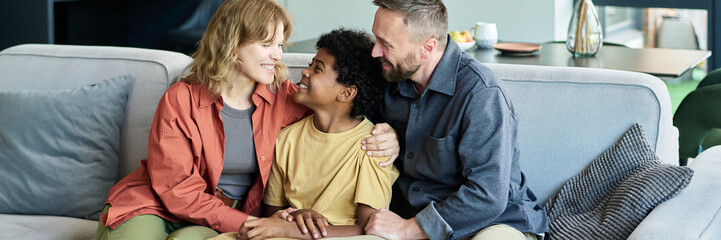 Family spending quality time together on a cozy couch with warm smiles and embracing each other,...