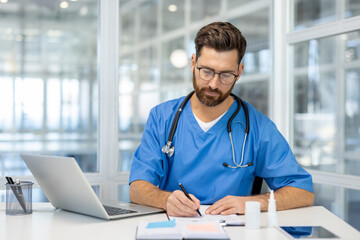 Fototapeta premium Doctor writing at desk with laptop, conveying professionalism and focus in healthcare environment. Modern office setting enhances theme of medical expertise and dedication.
