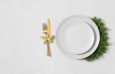 Christmas table setting with beige empty plate, fir branches and golden cutlery on white background. New Year serving for a festive dinner. Copy space. Directly above.
