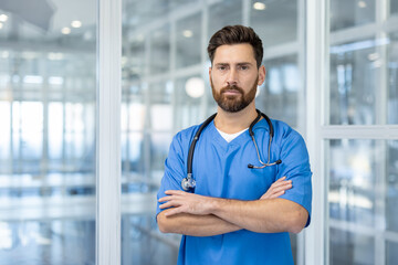 Confident male nurse wearing with stethoscope in modern hospital. He stands with arms crossed, portrays professionalism and trust in healthcare environment.