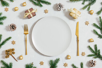 Beautiful Christmas table setting with golden cutlery and decorations, fir branches and gifts. Empty beige plate for New Year serving. View from above.