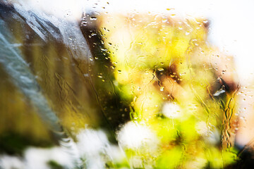 Rain water on car front wind screen with blurred green and yellow trees and a blurred building 