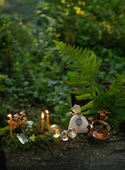 witch cauldron, magic bag, burning candles and crystals on tree trunk in forest, natural dark...