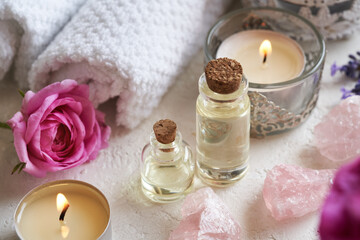 Two bottles of aromatherapy essential oil with fresh rose de Mai flowers, rose quartz stones and spa towels