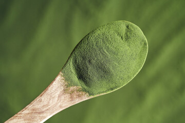 Green chlorella algae powder on a wooden spoon, top view