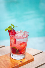 Strawberry mojito in a glass with slice strawberries, mint leaves on a wooden surface near a pool