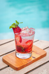Strawberry mojito in a glass with slice strawberries, mint leaves on a wooden surface near a pool