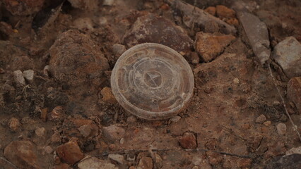 A discarded plastic lid lies on rocky, dusty ground outdoors.