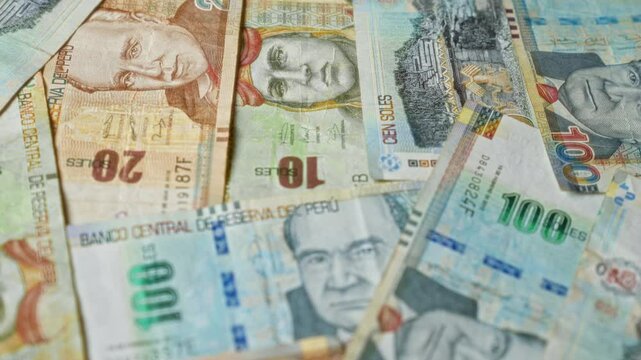 Peruvian banknotes arranged in a scattered manner showcase various denominations including 10, 20, 100 soles with prominent historical figures.