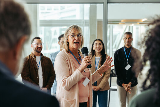 Confident female speaker leading a training session with engaged employees in a modern office environment, promoting professional growth and team building