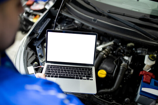 Mechanic using blank screen laptop to diagnose car engine issues in auto repair shop during daytime