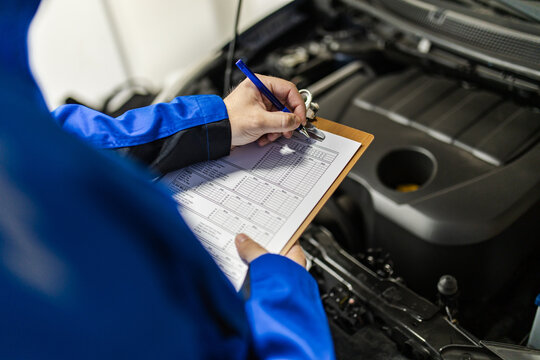 Mechanics perform maintenance check on vehicle engine while taking notes on clipboard