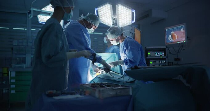 Medical Team Performing a Complex Surgery on a Patient, Using Specialized Tools, Looking at Digital Screens with Health Information. Doctors with a Female Surgeon in the Lead Saving Patient's Life