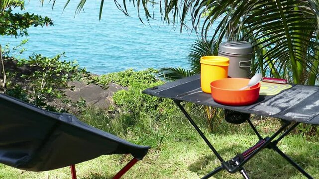 A set of camping utensils for the hike stands on the table, ultralight camping kitchen for cooking , in nature with a tropical view, folding chair and table