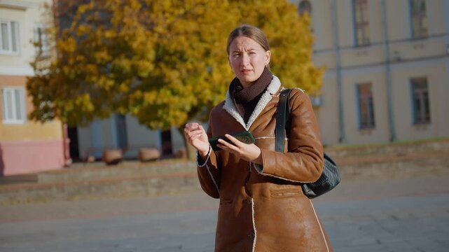 Young woman in brown jacket expressing sadness and anxiety, she is lost and worried can't find her way from maps on her phone. Urban environment intensifies her emotional struggle, loneliness sadness