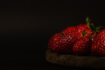 Strawberries on a wooden board with a black background.