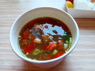 Close up of Soto Ayam Medan or Indonesian style chicken soup in white kraft paper bowl isolated on wooden background.