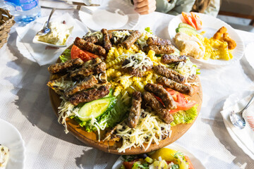 Mouthwatering platter of grilled meat, a popular Balkan dish, served with fries, vegetables, and cheese at the restaurant.