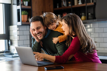 Happy young family with kids in kitchen have fun using modern laptop together, enjoying weekend