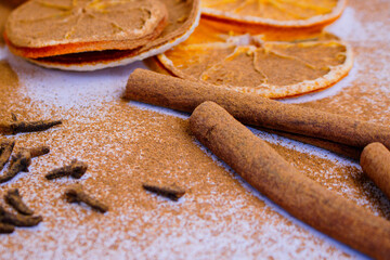 A pile of orange slices and cinnamon sticks on a white background. The oranges are cut in half and the cinnamon sticks are whole. Concept of warmth and comfort