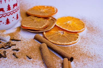 A pile of orange slices and cinnamon sticks on a white background. The oranges are cut in half and the cinnamon sticks are whole. Concept of warmth and comfort