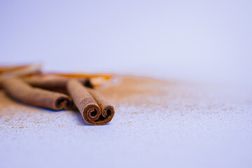 A pile of orange slices and cinnamon sticks on a white background. The oranges are cut in half and the cinnamon sticks are whole. Concept of warmth and comfort