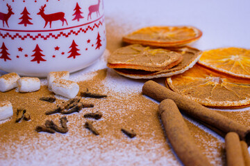 A pile of orange slices and cinnamon sticks on a white background. The oranges are cut in half and the cinnamon sticks are whole. Concept of warmth and comfort