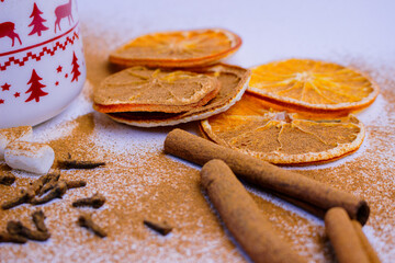 A pile of orange slices and cinnamon sticks on a white background. The oranges are cut in half and the cinnamon sticks are whole. Concept of warmth and comfort