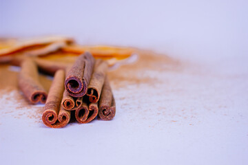A pile of orange slices and cinnamon sticks on a white background. The oranges are cut in half and the cinnamon sticks are whole. Concept of warmth and comfort