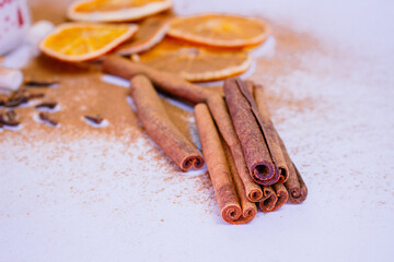 A pile of orange slices and cinnamon sticks on a white background. The oranges are cut in half and the cinnamon sticks are whole. Concept of warmth and comfort