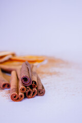 A pile of orange slices and cinnamon sticks on a white background. The oranges are cut in half and the cinnamon sticks are whole. Concept of warmth and comfort