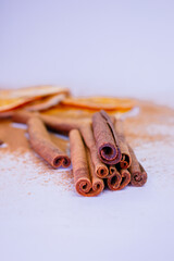A pile of orange slices and cinnamon sticks on a white background. The oranges are cut in half and the cinnamon sticks are whole. Concept of warmth and comfort